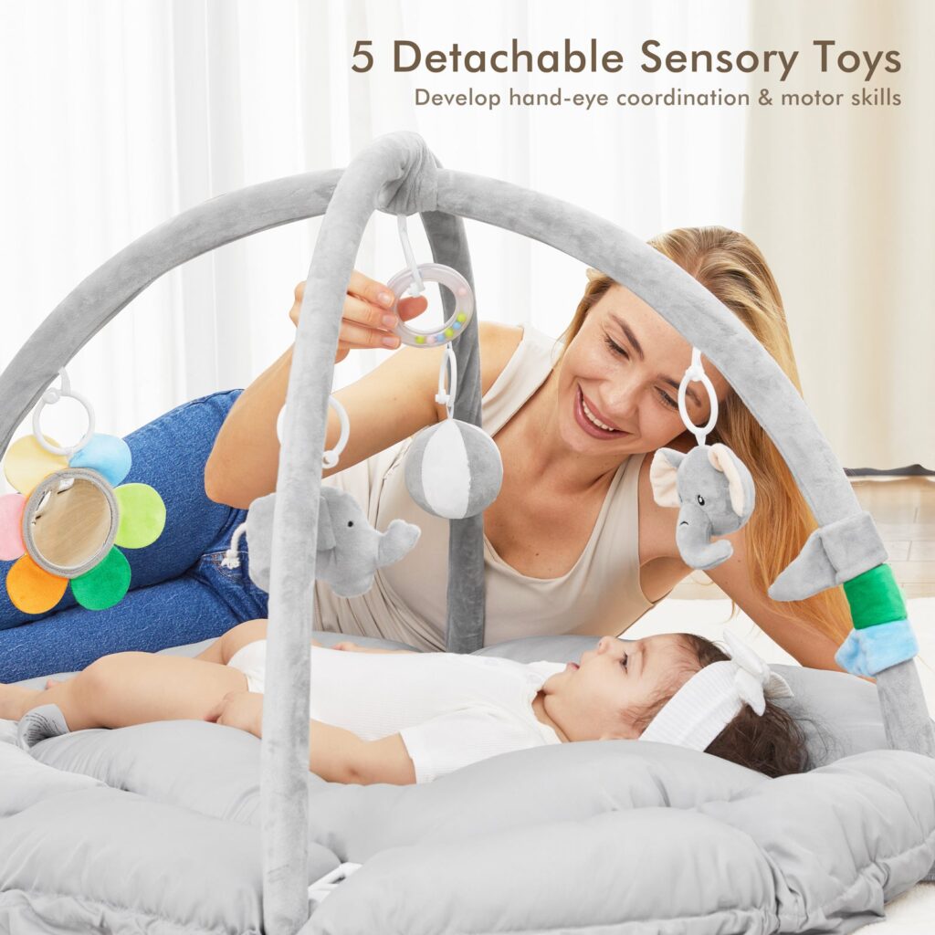 Parent lying beside a baby under the Angelbliss play gym, pointing to the hanging toys