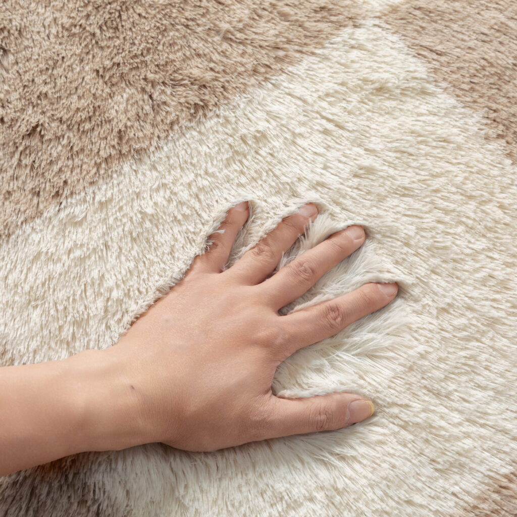 Hand pressing into the soft cream and tan pile of a shag rug