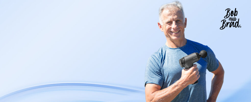 Man holding a Bob and Brad massage gun and smiling outdoors under a clear sky