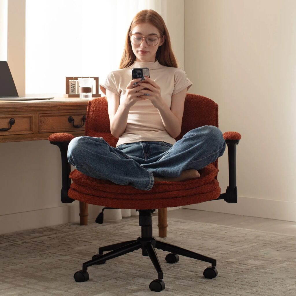 Person sitting cross-legged on a rust-colored Dowinx office chair at a wooden desk