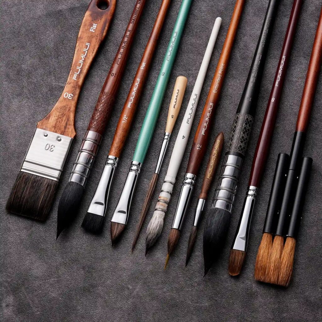Fuumuui brushes in different hair types and shapes on a dark gray surface, from a wide flat wash brush to fine detail rounds