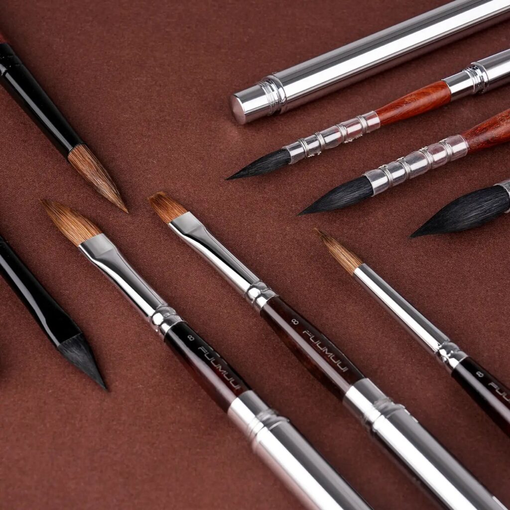 Fuumuui travel brushes with natural hair tips, silver ferrules and a metal cap on a brown surface
