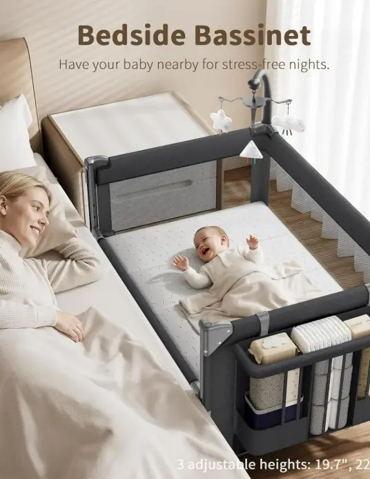 Gaive bedside bassinet pushed against an adult bed, with a baby lying on the mattress under a toy mobile and a parent resting nearby