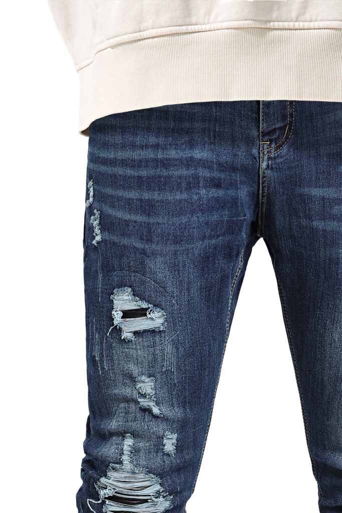 Studio close-up of the waist and thigh of dark blue ripped skinny jeans with black underlay behind the rips