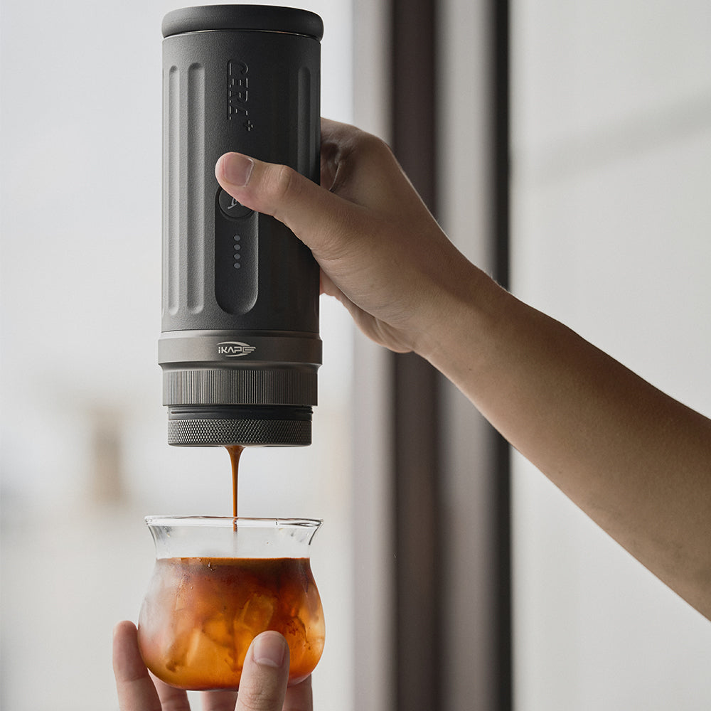 Hand holding an IKAPE Kapo K2 portable coffee maker over a glass of iced espresso
