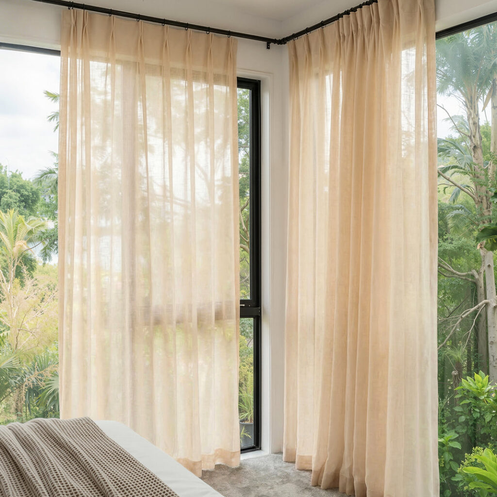 Sheer beige linen-blend curtains with pinch pleats filtering daylight in a corner window