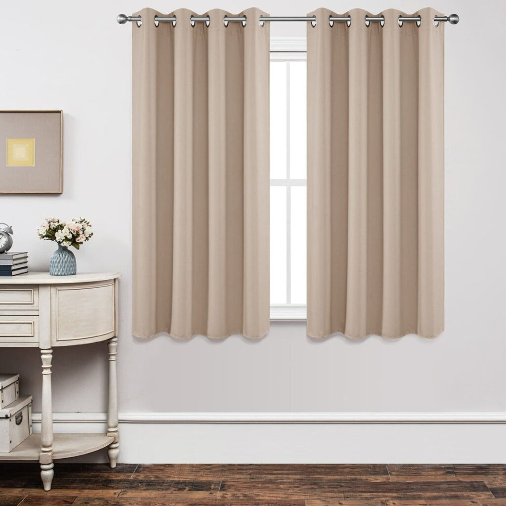 Beige Joydeco blackout curtains with silver grommets hanging on a silver rod beside a console table