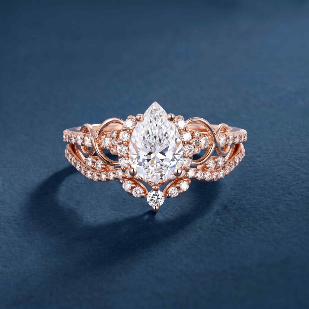 Pear-shaped diamond ring with a halo and a matching curved band in rose gold on a navy surface