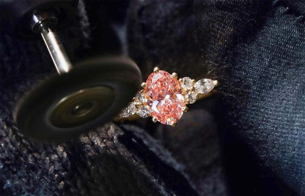 Oval pink stone ring in yellow gold beside a spinning polishing wheel