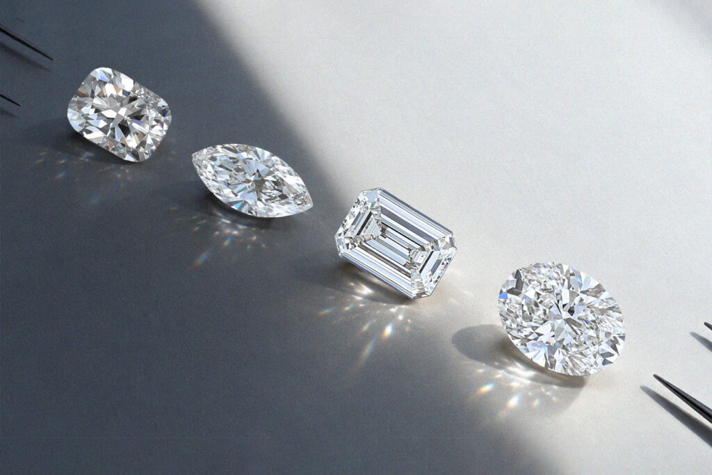 Four loose polished diamonds in cushion, marquise, emerald and oval shapes catching the light on a gray surface