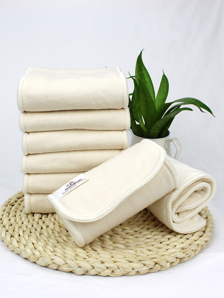 A stack of cream-colored Mama Koala bamboo cotton cloth diaper inserts on a woven mat