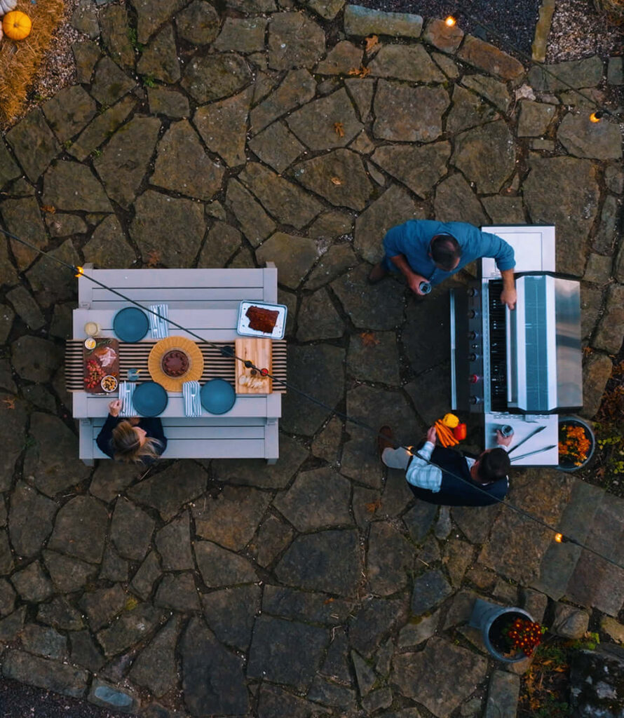 Overhead view of two people grilling beside a set dining table on a stone patio