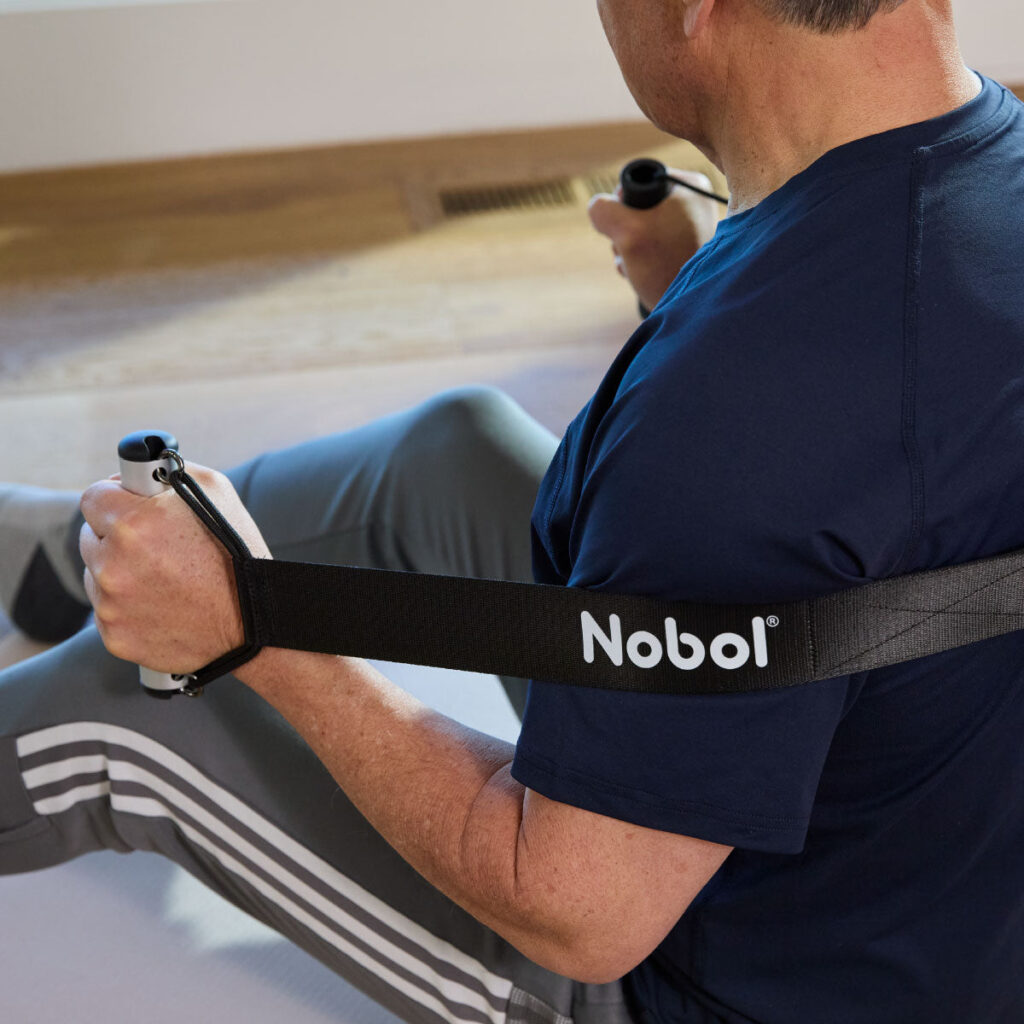 Man seated on a mat holding the handle of a black Nobol strap
