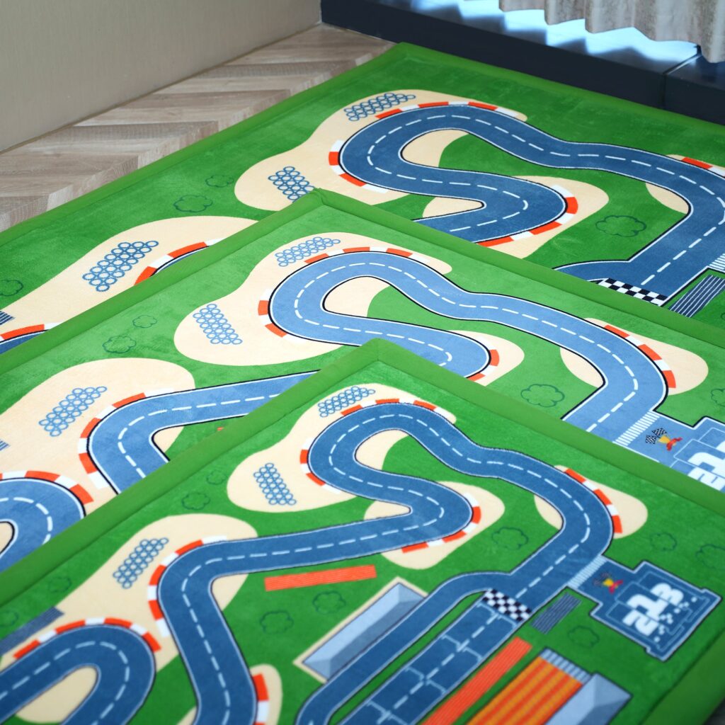 Three PaPaMat Race Track mats in different sizes stacked at the corners on a wood floor