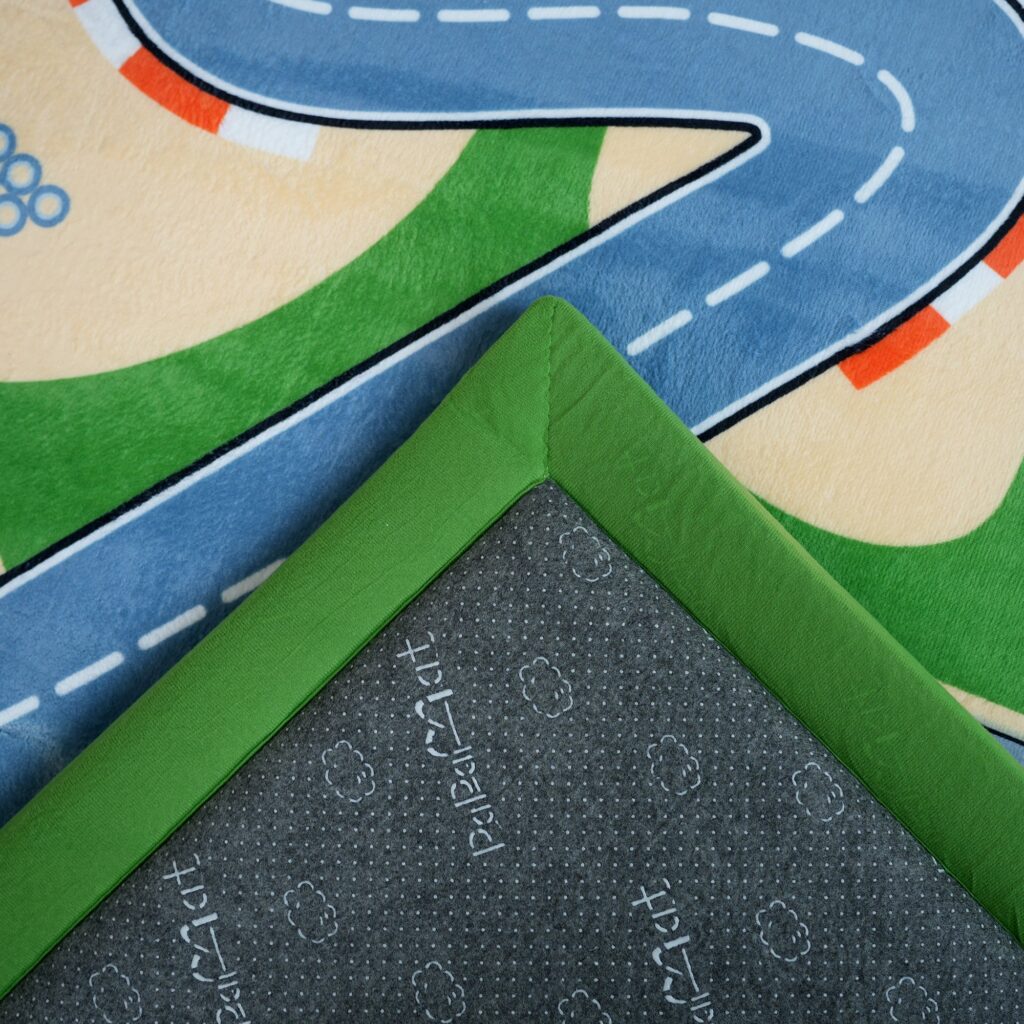 Corner of a PaPaMat Race Track mat turned up to show the grey dotted non-slip backing printed with the PaPaMat logo