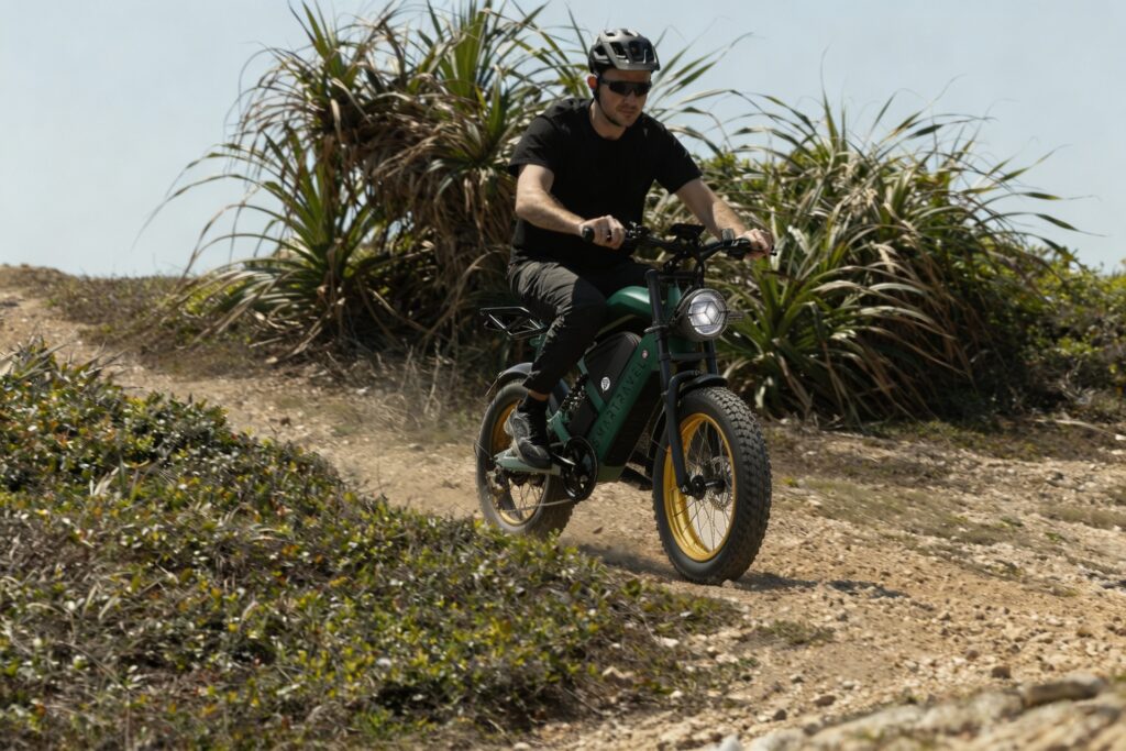 Rider on a green Smartravel e-bike riding down a dirt trail lined with tall coastal grass