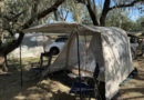Tentsla X1 pitched beside a Tesla under tall oak trees, with its front canopy held up on poles