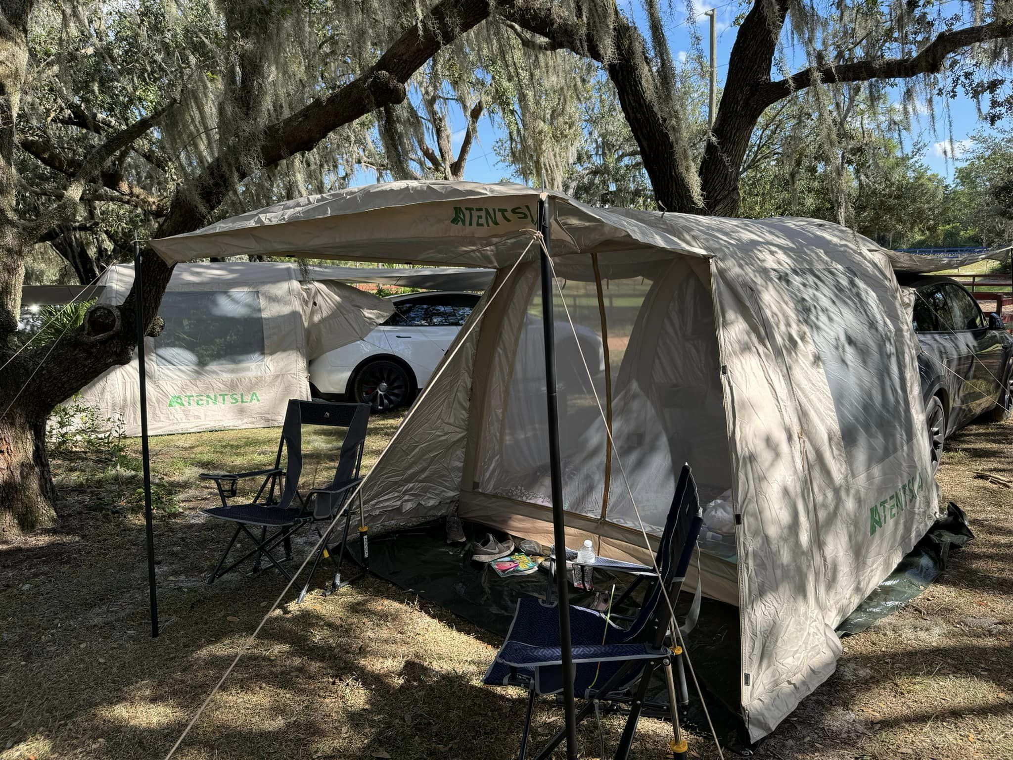 Tentsla X1 pitched beside a Tesla under tall oak trees, with its front canopy held up on poles