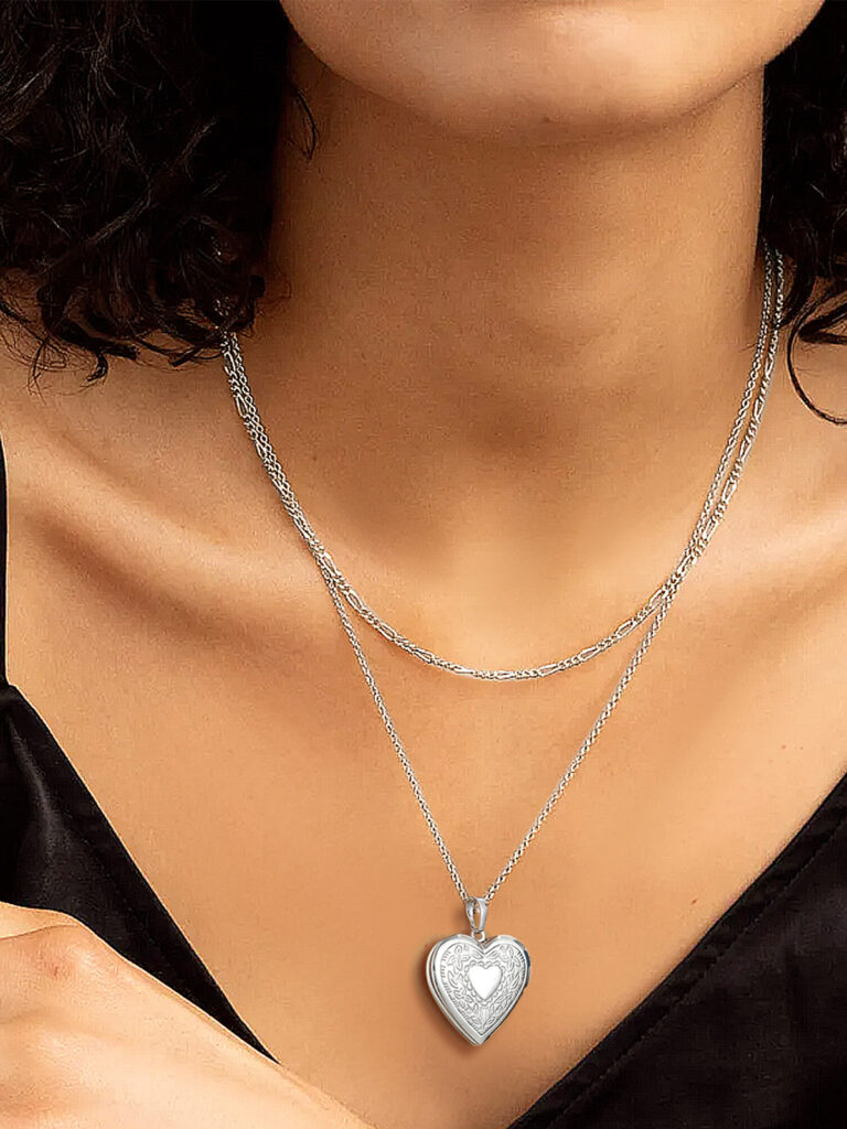 Model wearing a platinum heart locket on a long chain layered over a second, shorter chain